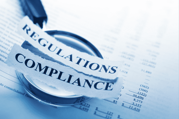 The words Regulations and Compliance over a balance sheet and magnifying glass